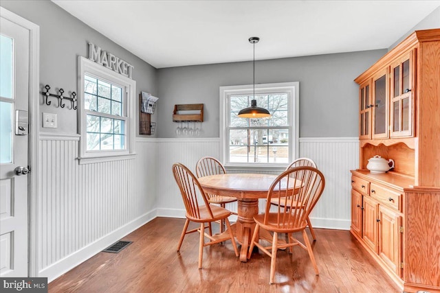 dining area with a wainscoted wall, light wood-type flooring, and visible vents