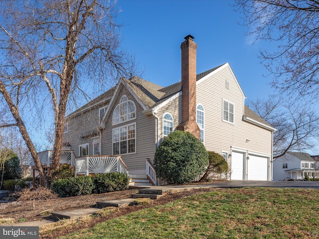 exterior space with an attached garage, a chimney, and driveway