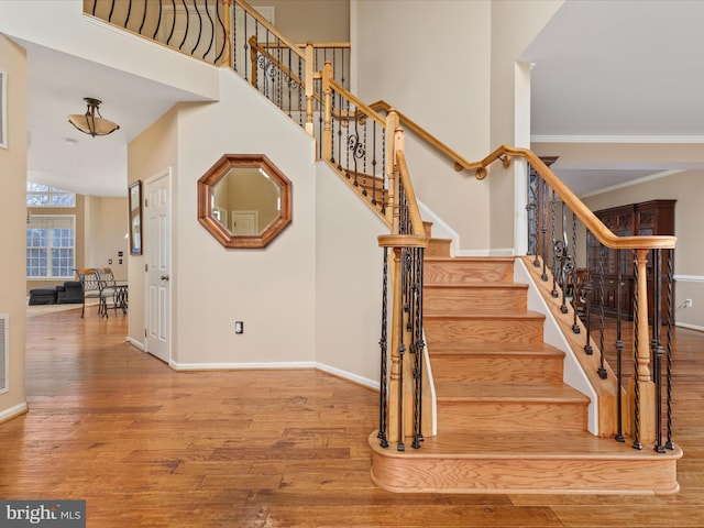 staircase featuring visible vents, baseboards, a towering ceiling, and wood finished floors