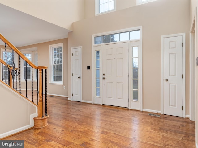 foyer entrance featuring visible vents, baseboards, stairs, a towering ceiling, and hardwood / wood-style flooring