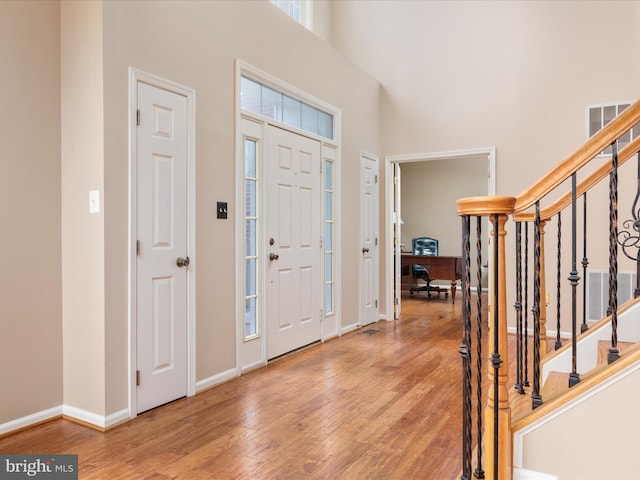 entryway featuring visible vents, baseboards, stairs, a towering ceiling, and wood finished floors