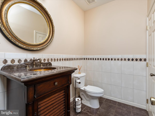 bathroom with vanity, tile walls, toilet, and a wainscoted wall