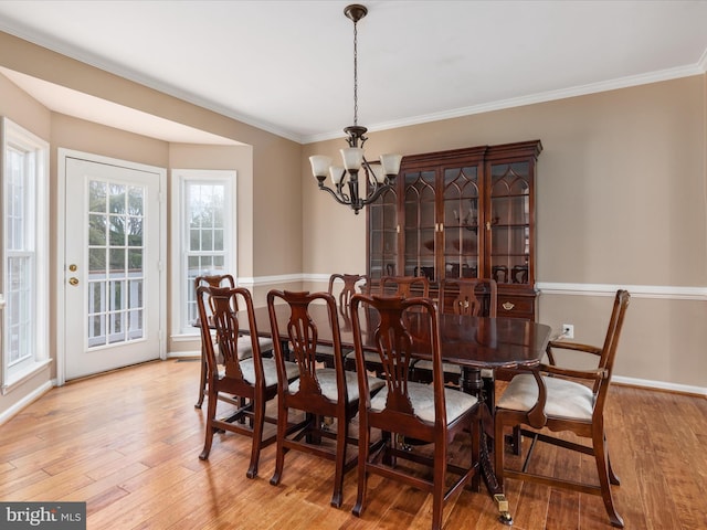 dining space with a notable chandelier, crown molding, and light wood-type flooring