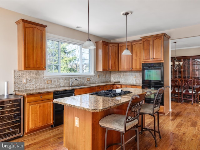 kitchen featuring beverage cooler, light wood-type flooring, brown cabinetry, black appliances, and a sink