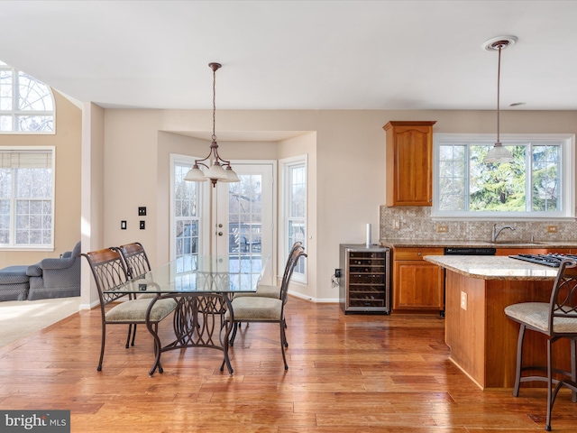 kitchen with light wood-style flooring, decorative backsplash, wine cooler, a kitchen breakfast bar, and brown cabinets