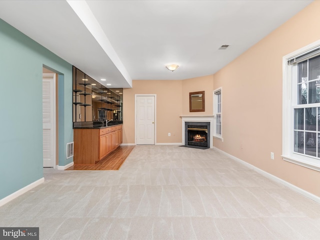 unfurnished living room with light carpet, visible vents, and baseboards