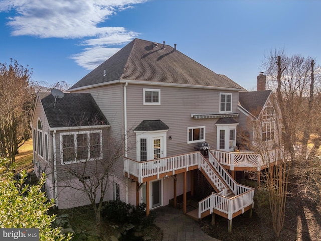 back of property featuring a deck, a patio area, a shingled roof, and a chimney