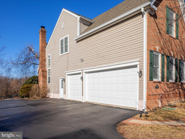 view of side of home featuring aphalt driveway, brick siding, and an attached garage