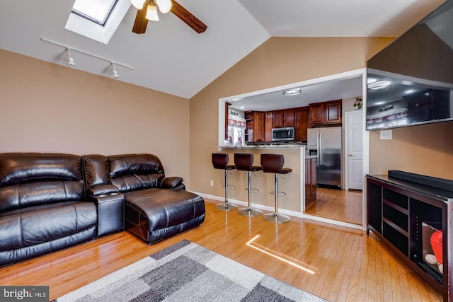 living room with ceiling fan, vaulted ceiling with skylight, track lighting, and light wood-type flooring