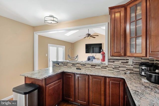 kitchen with light stone counters, lofted ceiling, kitchen peninsula, and decorative backsplash