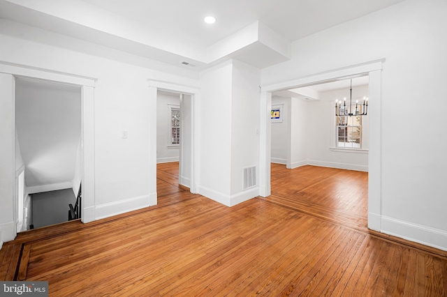 empty room with wood-type flooring and a notable chandelier