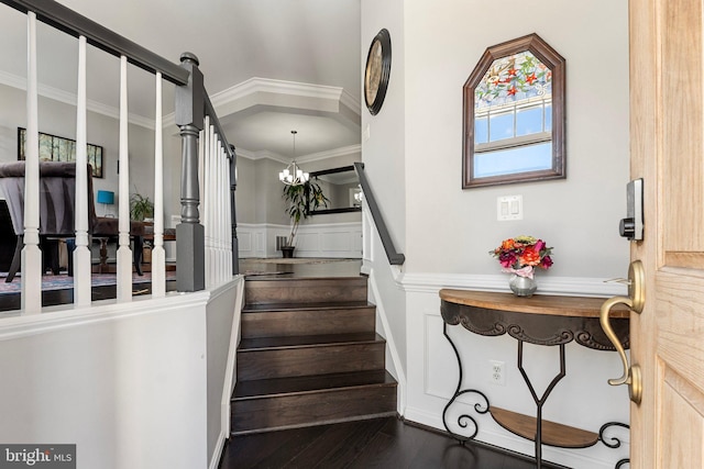 staircase featuring wainscoting, ornamental molding, a notable chandelier, and wood finished floors