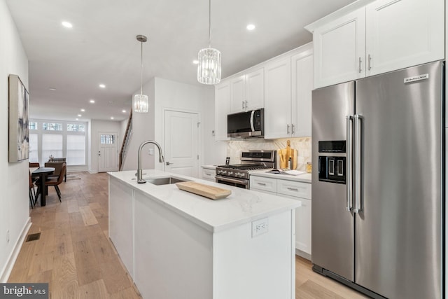 kitchen with sink, high end appliances, white cabinetry, decorative light fixtures, and a kitchen island with sink