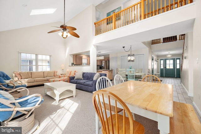 dining space with ceiling fan, a skylight, light hardwood / wood-style flooring, and a high ceiling