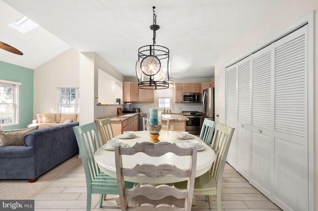 dining space featuring a healthy amount of sunlight, vaulted ceiling with skylight, and an inviting chandelier