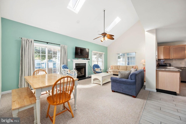 dining area with a skylight, high vaulted ceiling, light hardwood / wood-style floors, and ceiling fan