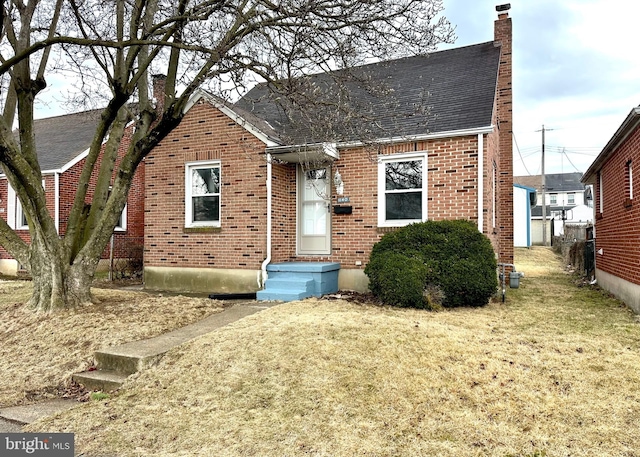 view of front facade with a shingled roof, brick siding, a chimney, and a front lawn