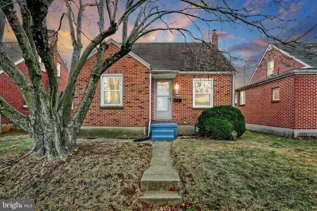 bungalow-style home featuring a shingled roof, a front yard, brick siding, and a chimney