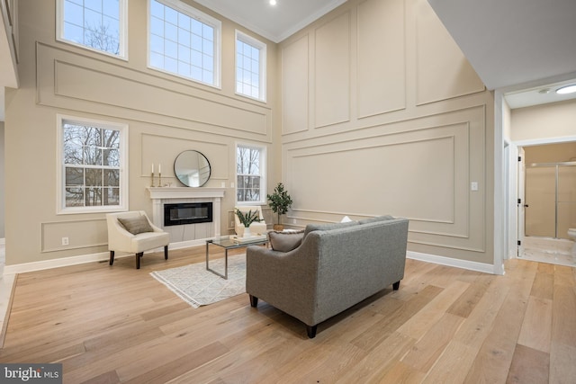 living room with a high end fireplace, ornamental molding, a high ceiling, and light wood-type flooring