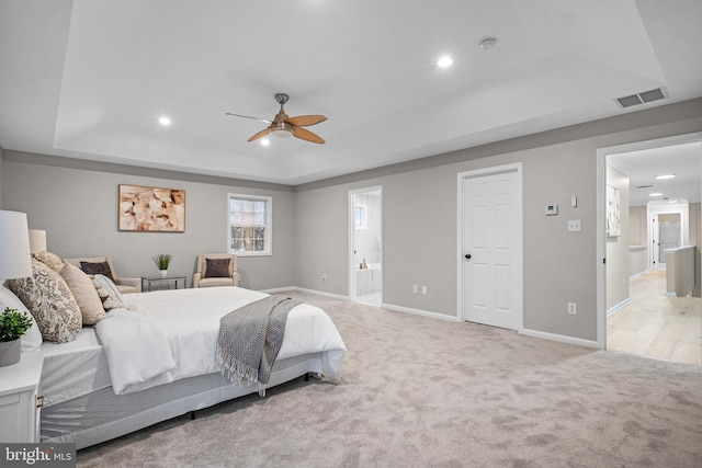 bedroom with ceiling fan, light colored carpet, connected bathroom, and a tray ceiling