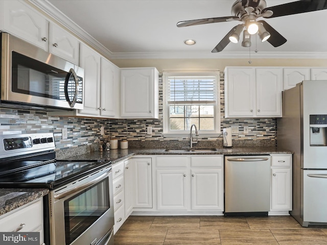 kitchen with appliances with stainless steel finishes, sink, white cabinetry, dark stone counters, and crown molding