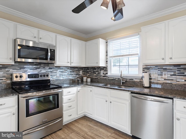 kitchen with stainless steel appliances, sink, dark stone countertops, white cabinets, and crown molding