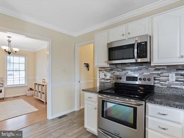 kitchen with appliances with stainless steel finishes, white cabinetry, crown molding, and dark stone counters