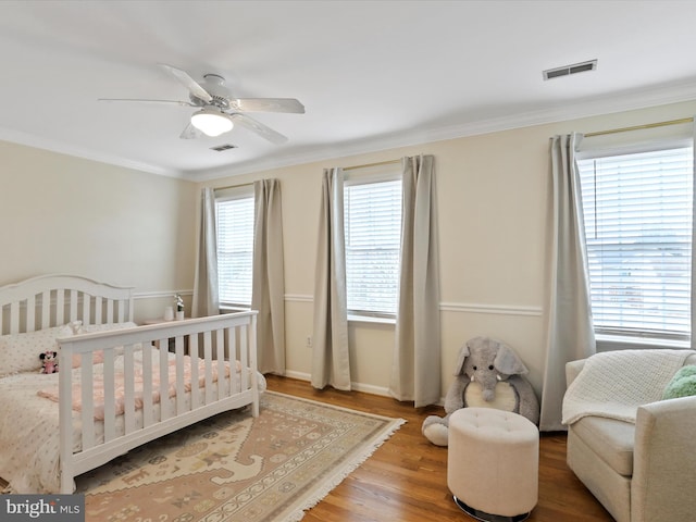 bedroom featuring ceiling fan, ornamental molding, wood-type flooring, and a nursery area