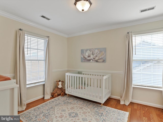 bedroom featuring ornamental molding, light hardwood / wood-style floors, multiple windows, and a crib