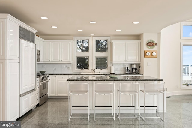 kitchen featuring premium appliances, a breakfast bar, white cabinets, and decorative backsplash