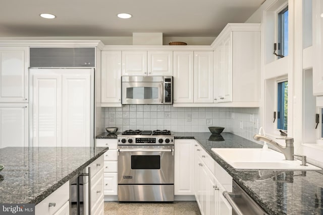 kitchen featuring appliances with stainless steel finishes, dark stone countertops, sink, and white cabinets