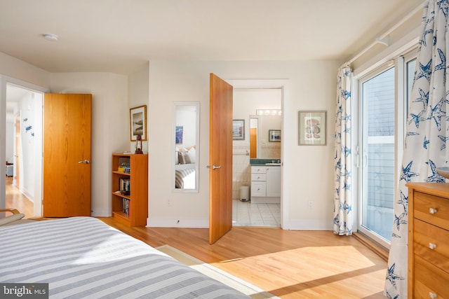 bedroom with ensuite bathroom, light hardwood / wood-style floors, and multiple windows