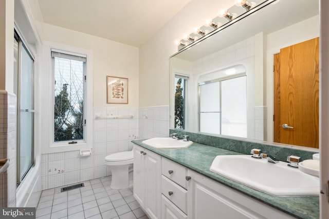 full bathroom with tile patterned flooring, vanity, enclosed tub / shower combo, toilet, and tile walls