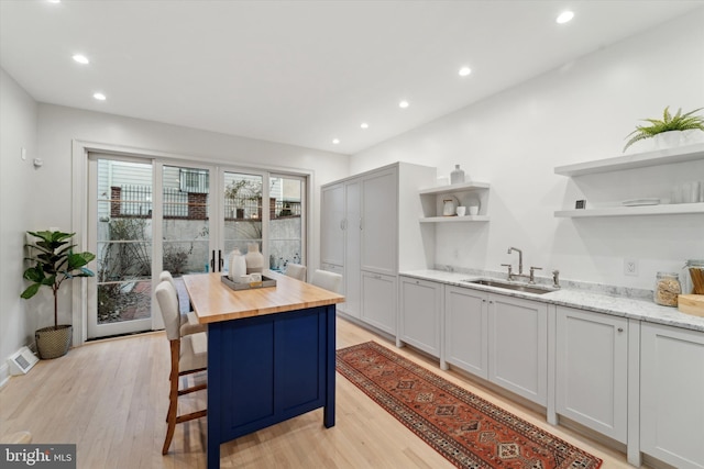 kitchen with a kitchen island, butcher block countertops, sink, a breakfast bar area, and light hardwood / wood-style floors