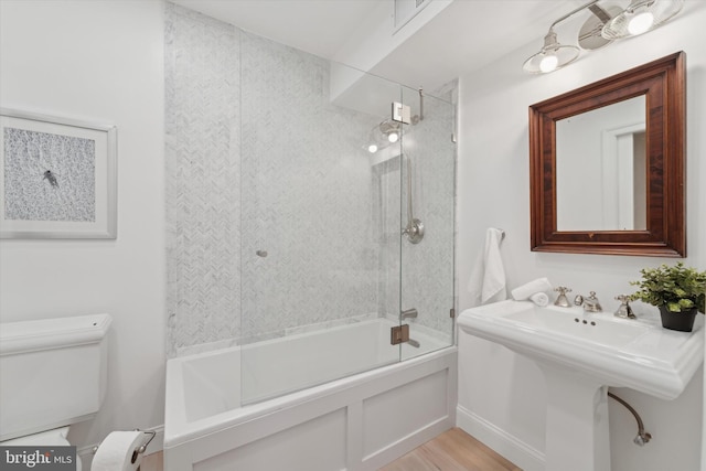 bathroom with combined bath / shower with glass door, hardwood / wood-style floors, and toilet