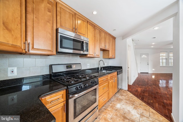 kitchen featuring stainless steel appliances, sink, backsplash, and dark stone counters