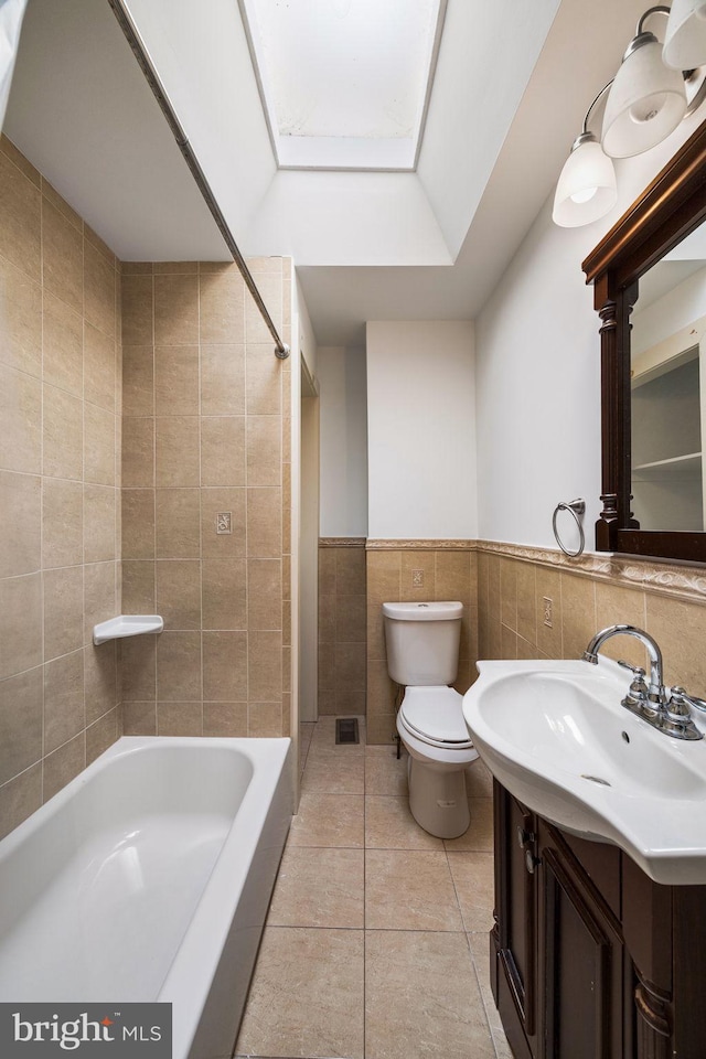 full bathroom featuring a skylight, tile walls, tile patterned flooring, vanity, and toilet