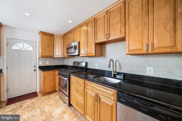 kitchen with backsplash, stainless steel appliances, sink, and dark stone countertops