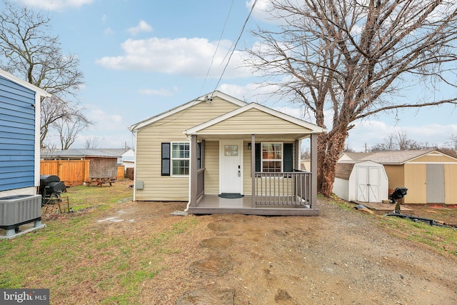 bungalow-style house featuring an outbuilding, a porch, central AC unit, a storage shed, and a front yard