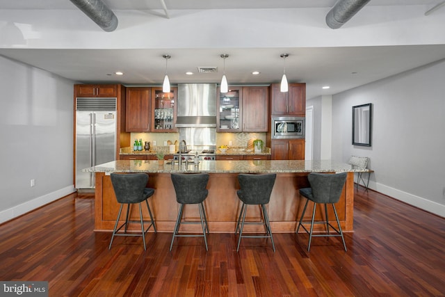 kitchen with built in appliances, wall chimney range hood, a large island, and hanging light fixtures