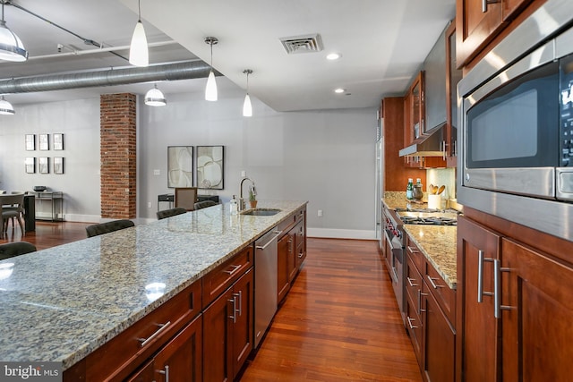 kitchen with sink, appliances with stainless steel finishes, hanging light fixtures, dark hardwood / wood-style floors, and light stone countertops