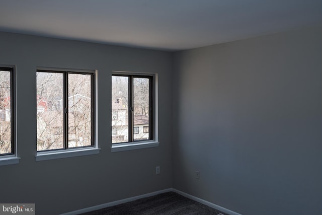 unfurnished room featuring baseboards and dark colored carpet