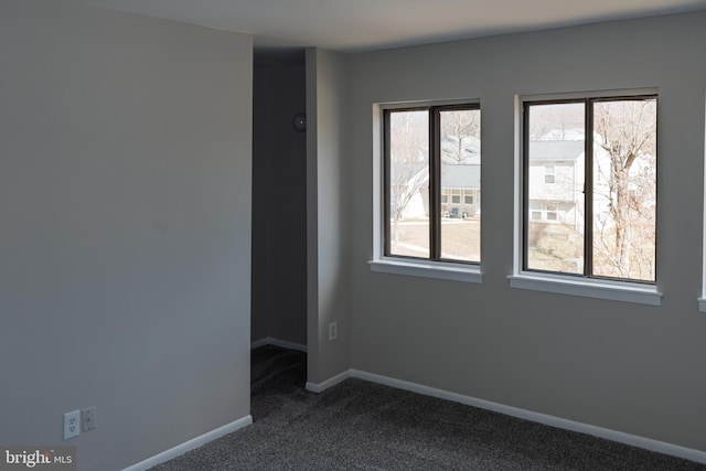 spare room featuring baseboards and dark carpet