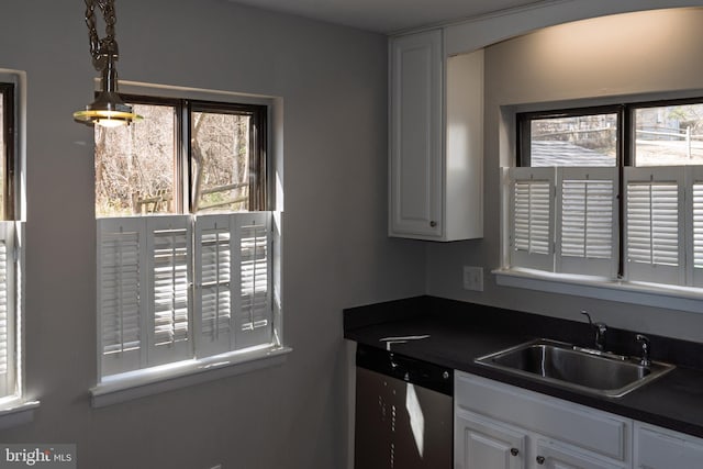 kitchen with dark countertops, dishwasher, hanging light fixtures, white cabinetry, and a sink