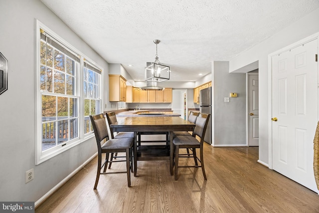 dining area with a notable chandelier, a textured ceiling, and light wood-type flooring