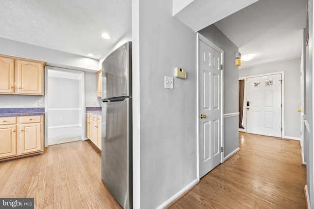 kitchen with light brown cabinets, stainless steel fridge, a textured ceiling, and light hardwood / wood-style flooring