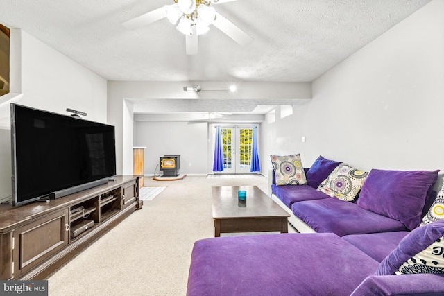 living room featuring a wood stove, a textured ceiling, ceiling fan, and french doors