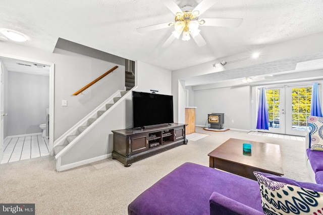 living room with a wood stove, ceiling fan, light carpet, a textured ceiling, and french doors