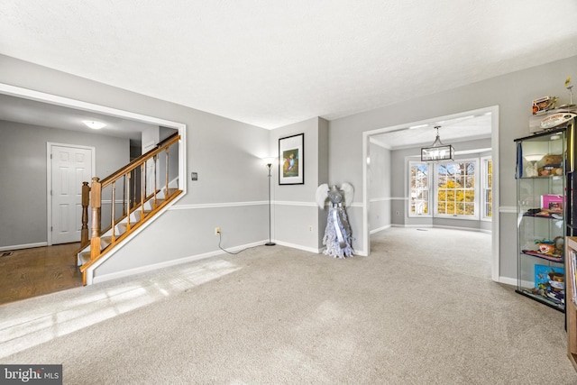 unfurnished room featuring a textured ceiling, carpet, and a notable chandelier