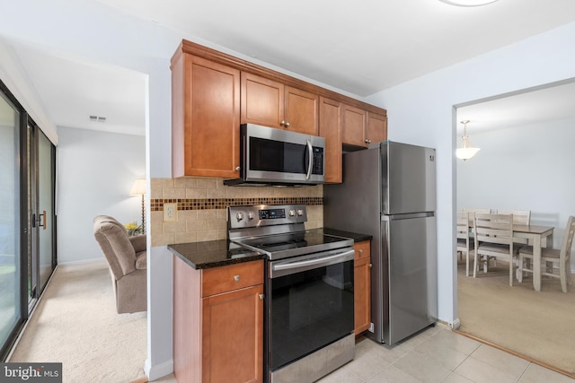 kitchen featuring tasteful backsplash, decorative light fixtures, appliances with stainless steel finishes, light colored carpet, and dark stone counters